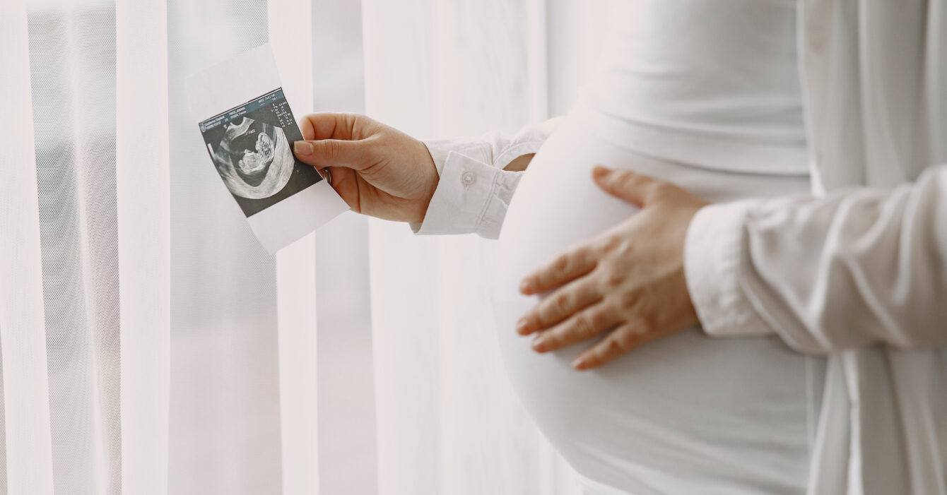 Pregnant woman stands by the window and looks at photo Pregnant woman stands by the window and looks at photo