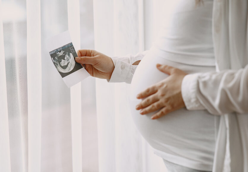 Pregnant woman stands by the window and looks at photo Pregnant woman stands by the window and looks at photo